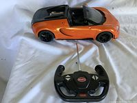 Photo showing the orange and black Bugatti remote controlled car next to its black controller with buttons and Bugatti logo.