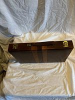 Closed view of the wooden backgammon case showing brown wood finish, leather handle, and brass latches.