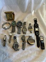 Overhead view showing assortment of wristwatches, folding travel alarm clock and pocket watch laid out on fabric