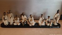 Front view of all eight Asian porcelain figurines arranged on a black wood base.