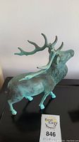 Side view of bronze elk statue showing the overall shape and detailed antlers with green patina.