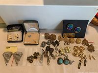 Overview of various pairs of costume jewelry earrings and a brooch arranged on a flat surface, showing different styles and colors.