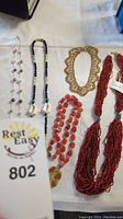 Lot of five necklaces with various bead and shell designs on white background.