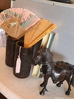 Photo showing two carved bamboo vases holding decorative oriental fans and a dark hardwood carved horse statue.