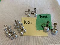 All three pairs of pearl earrings arranged on a fabric surface with notes showing markings and lot number.