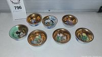 Photo of all 8 porcelain bowls showing gold interiors and various hand painted figures and patterns.