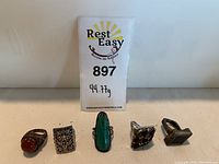 Photo showing the five silver rings with stones and designs on a flat surface with weight tag