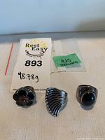 Three sterling silver rings front view on white surface with lot tag marked 893 and green .925 sticker