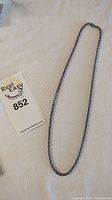 Full view of sterling silver chain laid out on fabric next to a label with auction or lot number.