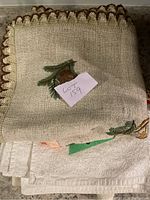 Folded beige linen with pine cone embroidery and crochet trim.