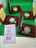 Set of 4 commemorative Canadian dollar coins in presentation cases with velvet red and black holders shown on green background.