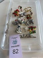 Top-down view of assorted cat jewelry on clear tray including brooches, pins, and pendant pieces with holiday themes and colorful details.