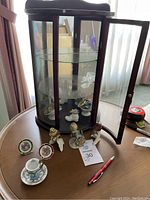 Curio cabinet with glass shelves showing bird figurines and decorative plates inside placed on wood table