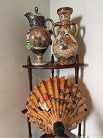 Photo showing decorative ceramic vase, porcelain pitcher, and parasol displayed on a wooden shelf