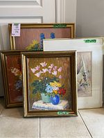 Four framed floral paintings, three oils and one watercolour, leaning against a wall