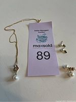 Photo showing gold chain necklace with a pendant pearl and two pairs of pearl stud earrings on a white surface with auction tag.