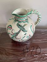 Full view of the ceramic jug showing overall shape, twisted handle, spout, and painted bird and floral motifs