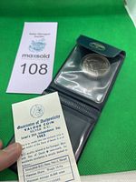 Photo of the coin in plastic holder alongside Guarantee of Authenticity certificate and auction tag.