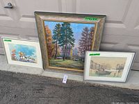 Three framed paintings leaning against garage door, showing size and condition details