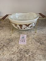 Pyrex 404 casserole dish with decorative brown and gold bird motifs, clear glass lid in metal holder with wooden handles, placed on kitchen counter.