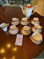 Overall view of 6 cups and saucers, the tall teapot, and creamer and sugar bowl set on a wooden table.