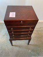 Full view of wooden silverware dresser on stand with multiple drawers and brass handles.