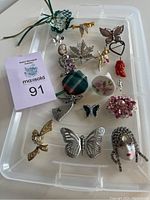 Full overview of the lot showing 15 brooches and pendants of various shapes and materials, including silver pieces, fabric tartan pin, enamel, and jewel accents.