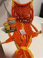 Macrame wall hanging in orange and yellow next to ceramic owl bank