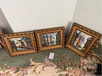 Photo showing three framed vintage oil paintings placed on a carpeted floor against a white wall.