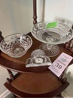 Three Waterford crystal pieces displayed on a wooden stand: small bowl, pedestal compote dish, and desk clock.