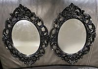 Photo showing two black oval mirrors with ornate decorative frames and carved detailing, placed side by side.