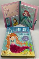 Photo showing the 5-Minute Enchanting Tales book with a mermaid on the cover and the Disney Princess Activity Pad featuring Ariel, all inside a pink folder-style packaging with card and character illustrations.