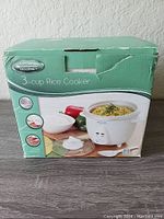 Original packaging box of Kitchen Gourmet 3-cup rice cooker showing product image and features.
