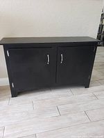 Front view of large black stand showing two closed doors with silver handles and smooth finish.