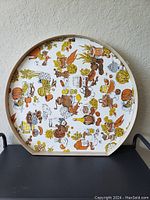 Front view of large round vintage serving tray with colorful fruit and kitchen motifs and wooden frame with handles