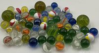 Top-down photo showing a spread of 53 vintage glass marbles in assorted colors and sizes on a white background.