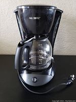 Front view of the black Mr. Coffee drip coffee maker showing the glass carafe and power cord coiled on the right side.