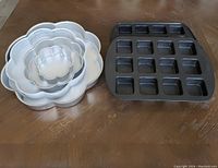 Five nested flower-shaped baking pans with one square compartment brownie pan to the right, all placed on a wooden surface.
