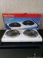Photo of the Betty Crocker Buffet Range Twin Burner with box in the background, showing two spiral coil burners on a white base.
