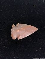 Close-up top view of reddish-brown agate arrow head with flaked edges and notched base.