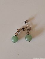 Two silver stud earrings with small silver bead and round pale green jade stone attached, showing front and side views.