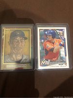 Pair of Christian Yelich baseball cards in protective sleeves, one Future Stars Rookie Card with modern photo and one Topps Gallery Impressionists art-style card.