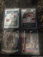 Four Lamelo Ball rookie cards in protective sleeves - Silver Prizm Crusade, Prizm Global Prospects, Optic Rated Rookie, numbered rookie card.