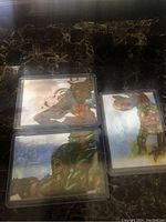 Three hologram Marvel Comics trading cards in protective plastic sleeves on a dark marbled surface.