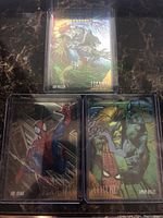 A golden web foil card of Lizard, along with Spider-Man and Vulture cards in protective sleeves on a marble surface.