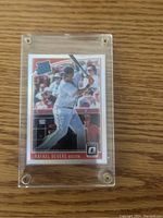 Front of Rafael Devers baseball card with Donruss Optic Silver Rated Rookie design in protective plastic case on wooden surface.