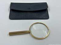 Black textured leather pouch with snap closure and gold-tone magnifying glass laid out