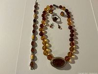 Main view of necklace, bracelet, ring, and two pairs of earrings laid out on white background