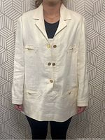 Front view of off-white linen jacket on mannequin showing notched collar, button closures and pockets.