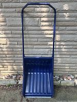 Front view of Garant XL snow shovel showing blue plastic scoop and adjustable blue metal handle against outdoor wall.
